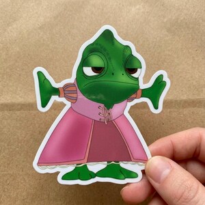 May include: A die-cut sticker featuring Pascal from Disney's Tangled. The green chameleon is depicted with a bored expression, wearing a pink dress with a matching bodice. The sticker has a white border and is held by a hand.