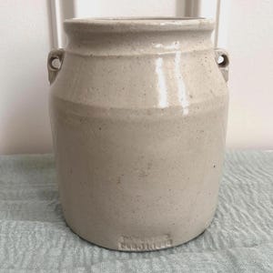 May include: A light beige ceramic crock with a cylindrical body, a slightly flared rim, and two small side handles. The surface has a speckled texture and the base features the embossed text "PATENTED FEB 1 1898" clearly visible on the front.