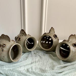 May include: Four speckled, light gray ceramic fish-shaped sculptures with open mouths and dark brown interior accents. Each piece features a dorsal fin, circular eye details, and small perforated holes along the sides, crafted with a smooth, glazed finish.