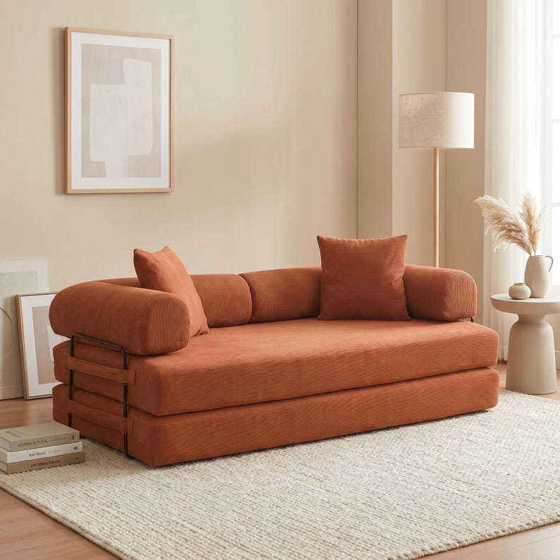 Modern green convertible folding sofa bed with ribbed corduroy fabric in a minimalist living room, featuring modular foam design, removable backrests, matching pillows, beige rug, and soft neutral decor near a large window.