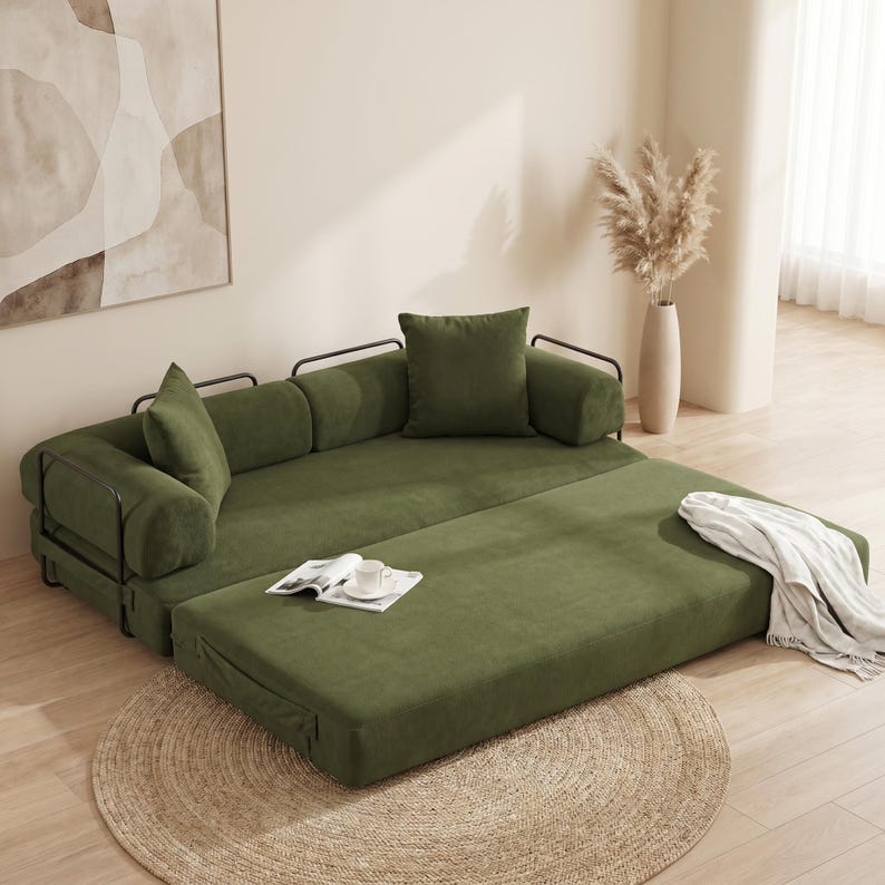 Modern green convertible folding sofa bed with ribbed corduroy fabric in a minimalist living room, featuring modular foam design, removable backrests, matching pillows, beige rug, and soft neutral decor near a large window.