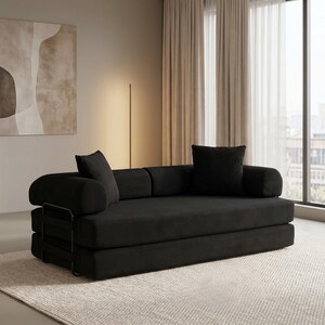 Modern green convertible folding sofa bed with ribbed corduroy fabric in a minimalist living room, featuring modular foam design, removable backrests, matching pillows, beige rug, and soft neutral decor near a large window.