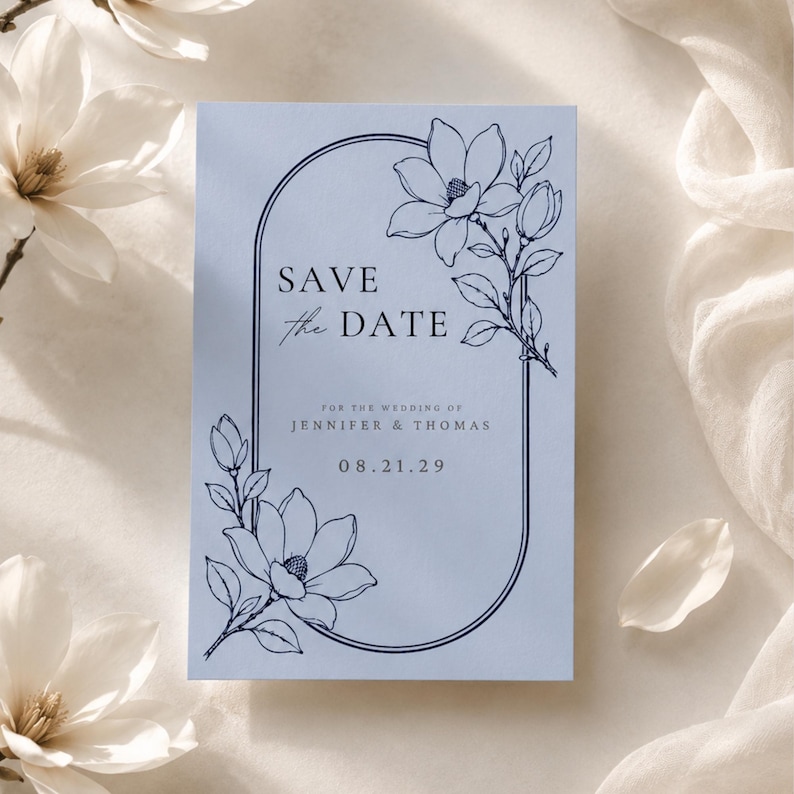 May include: A light blue rectangular Save the Date card featuring a dark blue arched frame and line art of magnolia flowers. The text reads: SAVE the DATE, FOR THE WEDDING OF JENNIFER & THOMAS, 08.21.29. The design includes floral accents.