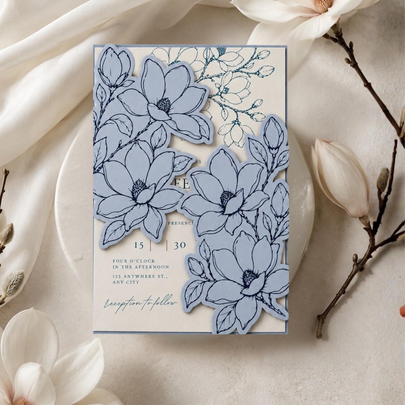 May include: A rectangular invitation card featuring a cream-colored background with dark blue line-art floral patterns. Two die-cut, light blue floral overlays are attached to the front, displaying text including 15, 30, four o'clock, and address details.