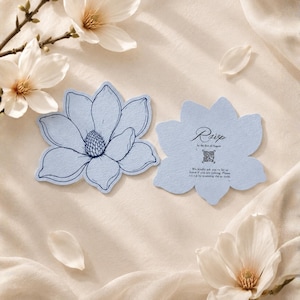 May include: Two light blue, flower-shaped cards with dark blue ink. One card features a detailed line drawing of a magnolia blossom. The other card displays the text RSVP by the first of August, a QR code, and instructions to scan the code.