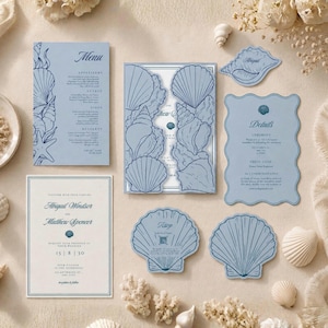 May include: A wedding stationery set featuring light blue paper with dark blue line art of seashells. The set includes a rectangular menu, a gatefold invitation, a scalloped details card, a rectangular invitation, and two shell-shaped RSVP cards.