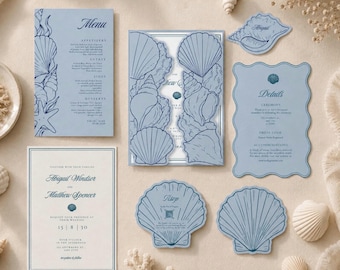 Puede incluir: Un juego de papelería de boda en papel azul claro con ilustraciones de conchas en azul oscuro. Incluye un menú rectangular, una invitación plegable, una tarjeta de detalles festoneada, una invitación rectangular y dos tarjetas RSVP.