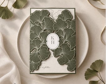 May include: A rectangular wedding invitation card featuring a dark olive green laser-cut overlay with a ginkgo leaf pattern. The center displays a white oval seal with the letters K and H. The inner card is cream-colored with visible text.