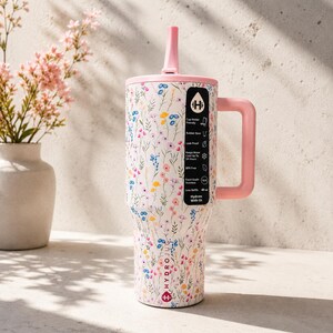 Puede incluir: Una botella de agua Hydrojug con estampado floral y asa y tapa rosas. La botella blanca est&aacute; cubierta de flores de colores y tiene una pajita rosa. La botella tiene un asa y una pegatina con informaci&oacute;n del producto.