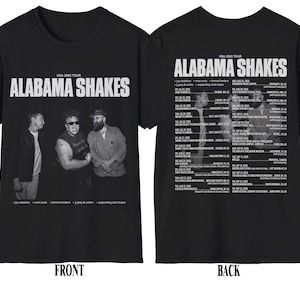 Può includere: Una t-shirt nera con una grafica frontale che riporta il testo Alabama Shakes e una fotografia in bianco e nero di tre persone. Il retro della maglietta mostra un elenco di date e luoghi del tour USA 2026 con il testo Alabama Shakes.