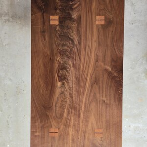 Puede incluir: Vista superior de una mesa rectangular de madera. La mesa es de madera marr&oacute;n oscura con un patr&oacute;n de vetas visible. Cuatro incrustaciones rectangulares de madera m&aacute;s clara est&aacute;n espaciadas uniformemente en la superficie, a&ntilde;adiendo un toque decorativo.
