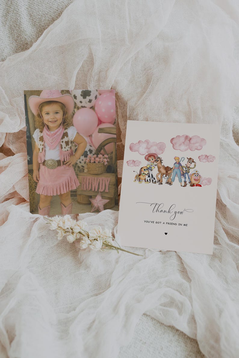 May include: A photograph of a young girl in a pink cowgirl outfit, and a greeting card with the text "Thank you". The card features a watercolor illustration of cartoon characters. The background is a soft, white fabric.