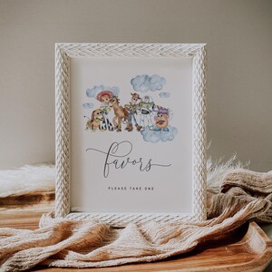 May include: White framed print with watercolour illustrations of animated film characters. The print includes the word "Favors" in cursive script, with the text "PLEASE TAKE ONE" below. The frame has a textured, carved design.