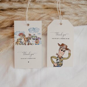 May include: Two cream gift tags with string. One tag features a cartoon of Woody, the cowboy, tipping his hat. The other tag has a cartoon of characters from Toy Story. Both tags have the text "Thank you, You've got a friend in me."