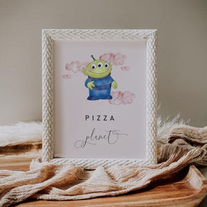 May include: A framed print featuring a cartoon alien character in a blue uniform, with three eyes and green skin, set against a pink cloud background. The words "PIZZA planet" are displayed in a playful font, perfect for a child's room or themed party.