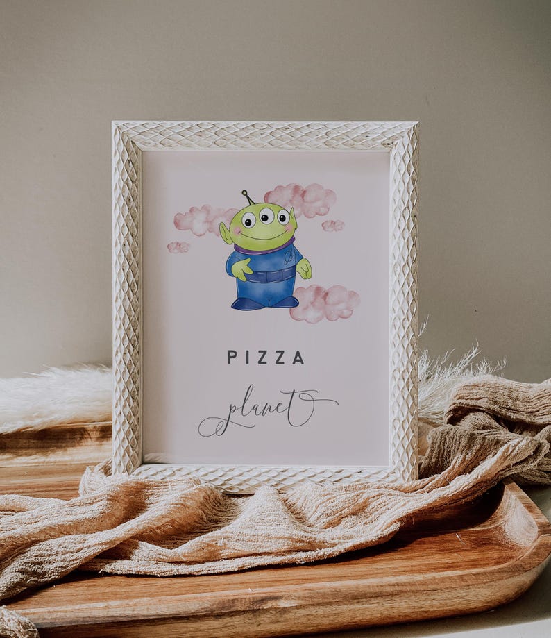 May include: A framed print featuring a cartoon alien character in a blue uniform, with three eyes and green skin, set against a pink cloud background. The words "PIZZA planet" are displayed in a playful font, perfect for a child's room or themed party.