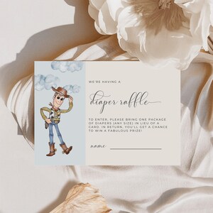 May include: A baby shower invitation card with a cartoon cowboy illustration. The card's text reads "We're having a diaper raffle". The card is light beige with a blue cloud background. The invitation is for a diaper raffle.
