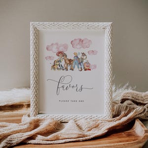 May include: White framed print with watercolor illustrations of cartoon characters and pink clouds. The word "favors" is written in cursive, with "PLEASE TAKE ONE" below. The frame has a textured, carved design.