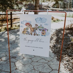 May include: A white sign featuring a watercolour illustration of Toy Story characters, including Woody and Buzz Lightyear. The sign reads "the gangs all here" and welcomes guests to Lucy's baby shower.