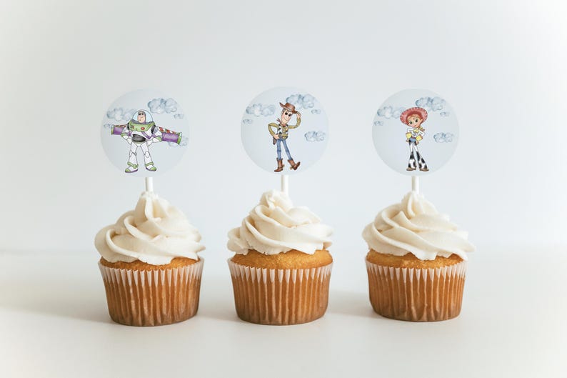May include: Three cupcakes with white icing, each topped with a circular image of a Toy Story character: Buzz Lightyear, Woody, and Jessie. The cupcakes are on a white surface, ideal for a themed party.