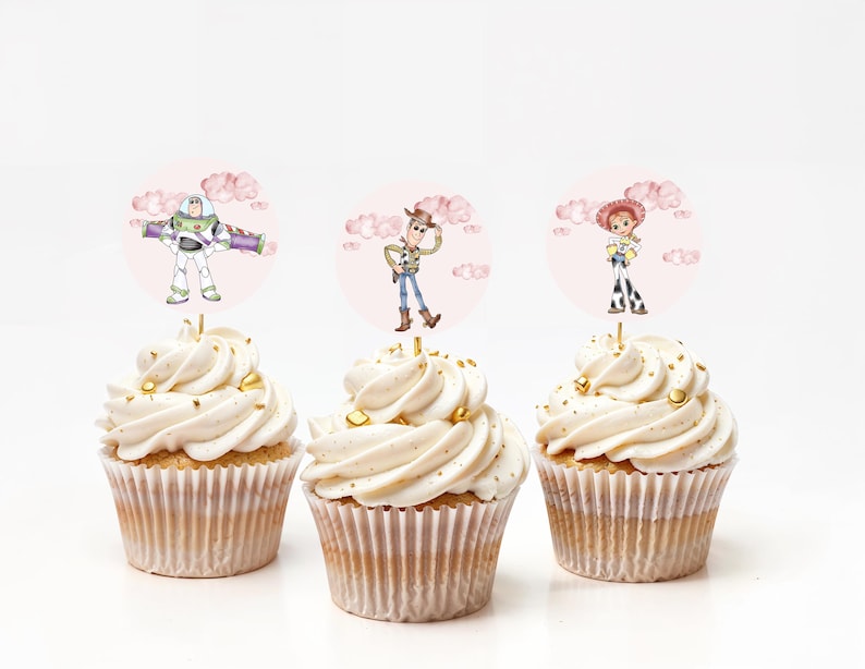 May include: Three cupcakes with white frosting and gold sprinkles. Each cupcake has a round topper featuring a character from the Toy Story movie: Buzz Lightyear, Woody, and Jessie. The toppers are set against a pink background with clouds.
