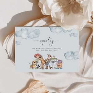 May include: A pale blue baby shower registry card featuring watercolour clouds and Toy Story characters. The card says "registry" in elegant script, with the text "The mom to be is registered at Baby Shower Boutique" beneath.