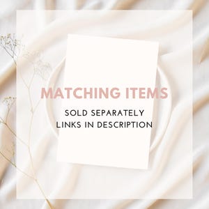 May include: A white card with the text "MATCHING ITEMS SOLD SEPARATELY LINKS IN DESCRIPTION" in pink, on a white plate. The background is a cream-coloured, draped fabric with a sprig of dried flowers.