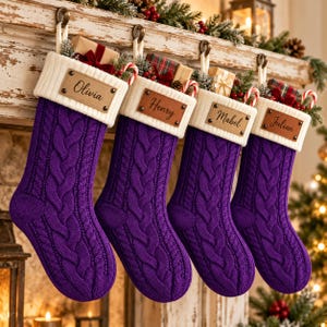 Puede incluir: Cuatro calcetines navideños de punto trenzado morado con puños acanalados blancos, cada uno con una etiqueta de cuero rectangular grabada con los nombres Olivia, Henry, Mabel y Julian, rellenos de pequeños regalos y bastones de caramelo.