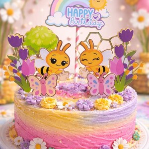 May include: A round cake with swirled pink, yellow, and purple frosting, decorated with small sugar flowers and a cake topper featuring two cartoon bees, two butterflies, purple tulips, and a rainbow sign that says Happy Birthday.