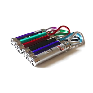 Op de afbeelding: Een verzameling laserpointers in verschillende kleuren, waaronder zilver, paars, groen, rood, zwart en blauw. Elke pointer heeft een zilveren metalen clip en een laserindicator. De pointers zijn in een rij gerangschikt, schuin.