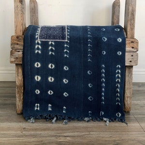Peut inclure: Un textile bleu et blanc à motifs plié sur un cadre en bois. Le textile a une bordure frangée et un motif géométrique.