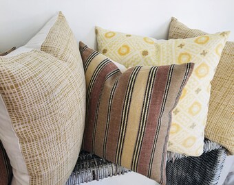 May include: Four decorative throw pillows with different patterns. The pillows are made of a soft, woven fabric. The patterns include a geometric design, a striped design, and a grid pattern. The pillows are arranged on a wicker surface.