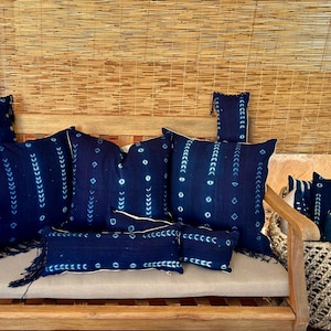 May include: A collection of blue and white patterned throw pillows with fringe on a wooden bench. The pillows are arranged in a variety of sizes and shapes.