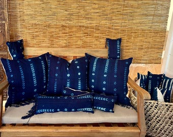 May include: A collection of blue and white patterned throw pillows with fringe on a wooden bench. The pillows are arranged in a variety of sizes and shapes.
