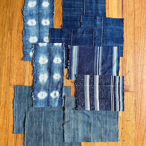Peut inclure: Un assortiment d'échantillons de tissu teints à l'indigo, présentant divers motifs. Les tissus comprennent des motifs à pois, à rayures et unis. Les pièces sont disposées sur une surface en bois, mettant en valeur les différentes textures et nuances de bleu.