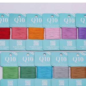 Könnte beinhalten: Eine Sammlung von Q10 by Nicolas Colors Perlenfadenkarten in verschiedenen Farben, darunter Rot, Pink, Orange, Hellrosa, Lila, Grün, Türkis, Blau, Grau und Beige. Jede Karte enthält den Text Q10, Nicolas Colors und 6 Meter.