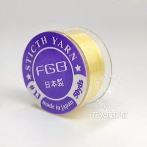 Può includere: Una bobina di filo giallo pallido etichettata STICTH YARN #13 50yds. L'etichetta circolare viola riporta il testo FGB, caratteri giapponesi e la dicitura made in japan. La bobina è in plastica trasparente e contiene un filo giallo sottile.