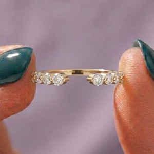 May include: A gold open-style ring featuring a row of small, round, clear stones set along each side of the band. The ring has a gap in the center, and the metal band is thin and polished, showcasing a bright, reflective gold finish throughout.