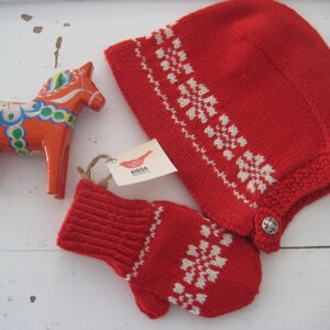 May include: Red knitted hat and mittens with a white snowflake pattern. The hat has a button on the side. A traditional Swedish Dala horse is also in the image.