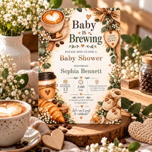 Peut inclure: Une carte d'invitation rectangulaire pour une fête prénatale avec des motifs sur le thème du café, incluant un latte avec de la mousse en forme de cœur, un croissant et des chaussons de bébé. Le texte indique Baby is Brewing et Sophia Bennett.