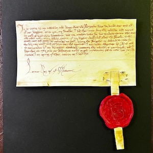 Könnte beinhalten: Ein gerahmtes Pergamentdokument mit handschriftlichem Text in roter Tinte, versiegelt mit einem roten Wachssiegel. Das Dokument ist gealtert, mit sichtbaren Knicken und einem vergilbten Aussehen, was auf historische Bedeutung hindeutet.