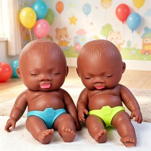 May include: Two dark-skinned baby dolls with closed eyes and tongues sticking out. They wear blue and yellow nappies. The dolls are sitting on a white surface, with a colourful balloon and cartoon-themed background.