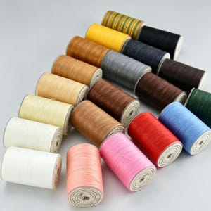 Può includere: Una collezione di rocchetti di filo in vari colori, tra cui bianco, rosa, rosso, blu, verde, marrone e giallo. I rocchetti sono disposti in diagonale, mostrando la diversa gamma di colori del filo.