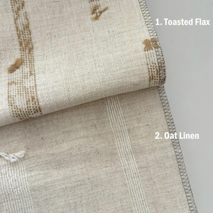 May include: Close-up of two linen fabrics. The top fabric, labeled "1. Toasted Flax," is a light beige with vertical brown embroidered stripes. The bottom fabric, labeled "2. Oat Linen," is a lighter beige with vertical white stripes. Both have gray stitched edges.