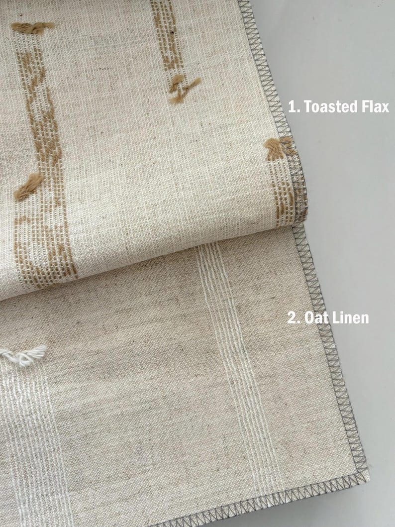May include: Close-up of two linen fabrics. The top fabric, labeled "1. Toasted Flax," is a light beige with vertical brown embroidered stripes. The bottom fabric, labeled "2. Oat Linen," is a lighter beige with vertical white stripes. Both have gray stitched edges.