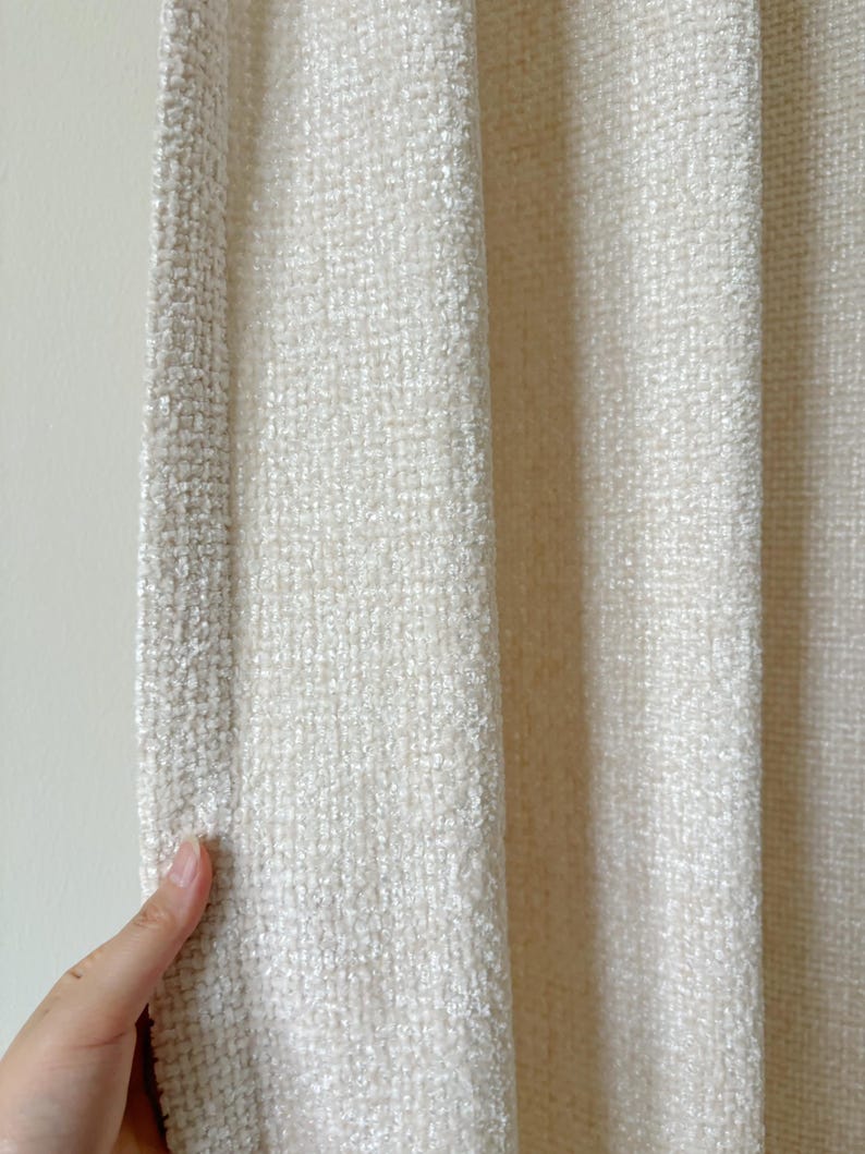May include: A cream-colored cardigan featuring a textured, woven fabric with a distinct grid-like pattern. The garment has a straight, open-front design with a reinforced edge along the vertical opening, showcasing a soft, slightly fuzzy surface texture.
