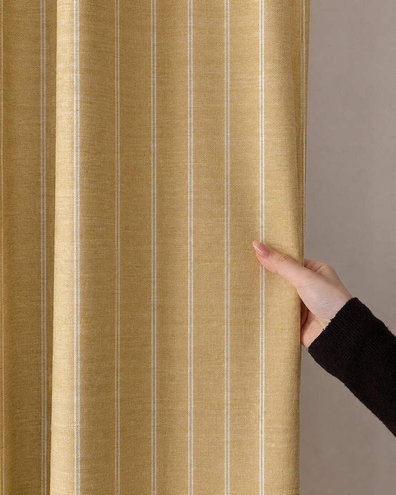 May include: Yellow and white striped fabric, likely a curtain or drapery. The fabric has vertical stripes of yellow and white. The texture appears to be woven. The image shows a section of the fabric being held.
