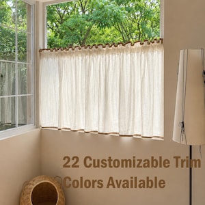 May include: A cream-colored cafe curtain featuring a gathered top with a brown trim and a matching brown hem. The curtain hangs in a window, and the text 22 Customizable Trim Colors Available is displayed in brown font over the wall.