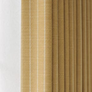 May include: Close-up of a tan fabric with vertical white stripes. The fabric is folded in a pleated style, creating a textured appearance. The color is a warm, neutral tone, suitable for home decor.