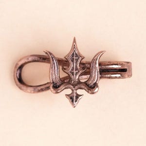 Könnte beinhalten: Eine kupferfarbene Metall-Krawattenklammer mit einem dreizackigen Emblem, das mittig auf einer horizontalen Leiste sitzt. Das Dreizack-Design hat eine texturierte, verwitterte Oberfläche mit einer spitzen Oberseite und geschwungenen Seitenzinken.